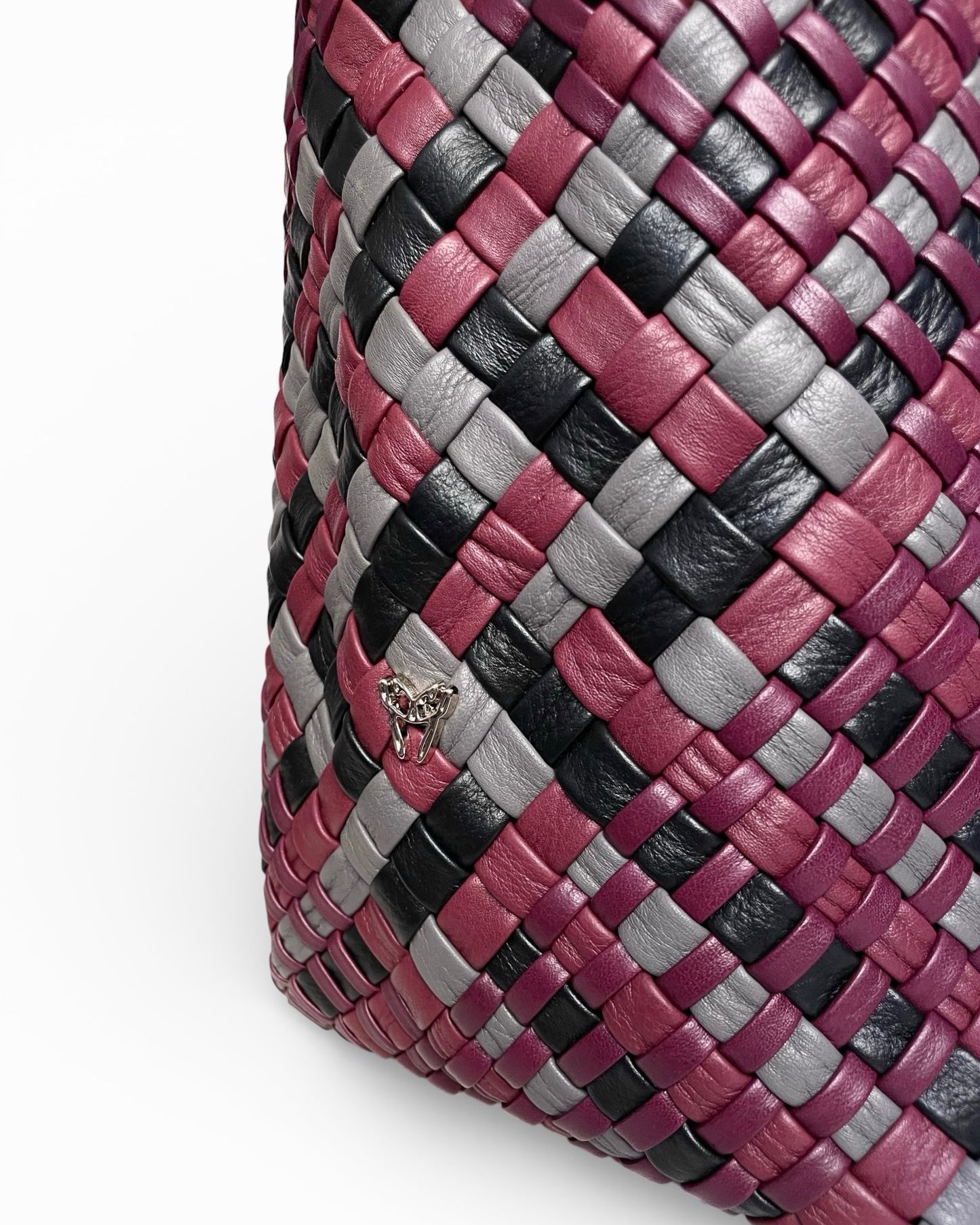Close-up of a woven leather product with a pattern of pink, black, and gray on a white background.