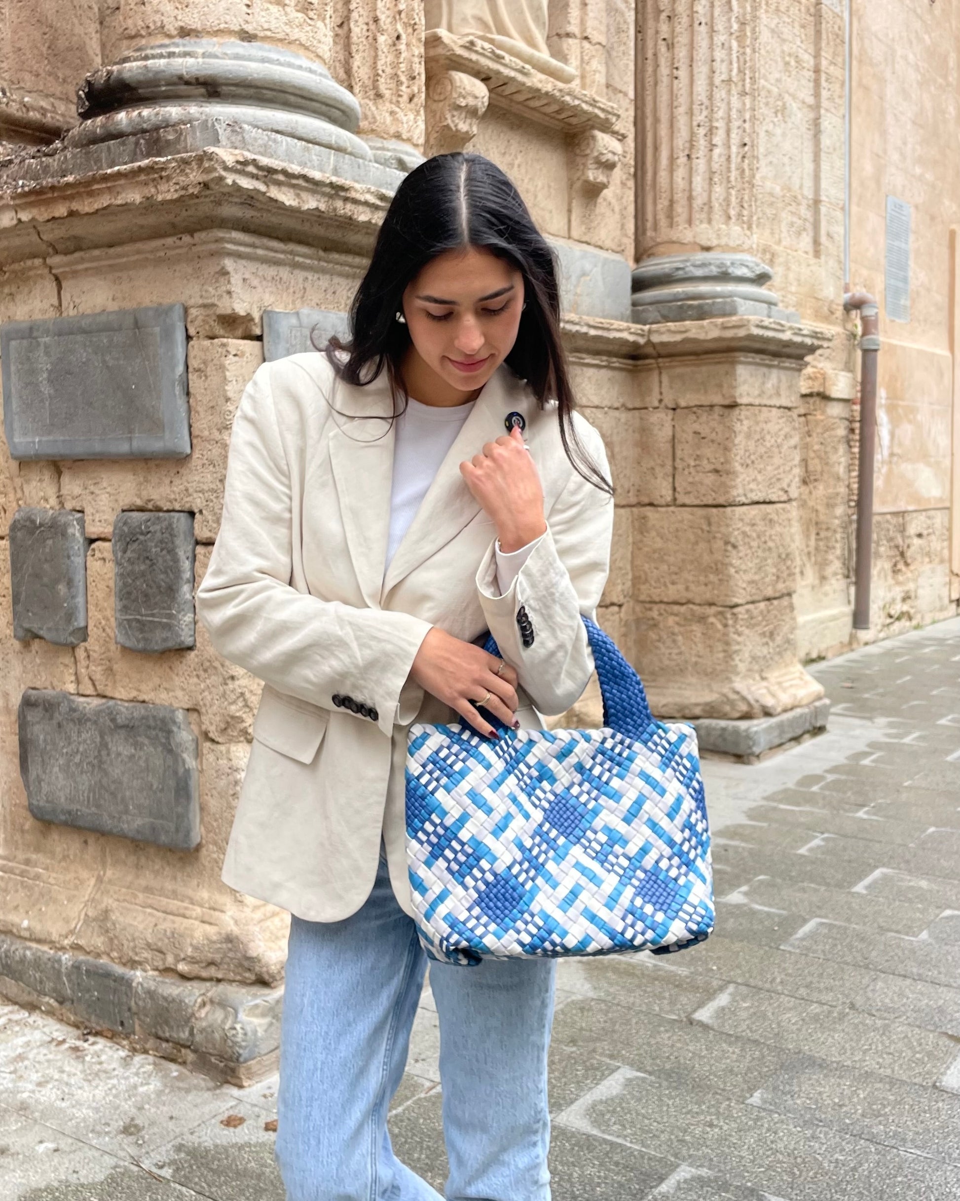 Woman holding a blue and white patterned bag in front of a stone building.